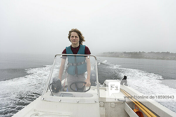 Boy (14-15) steering motorboat on foggy lake