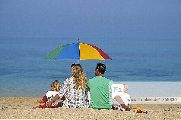 Paar mit 2 Kindern unter Sonnenschirm am Strand