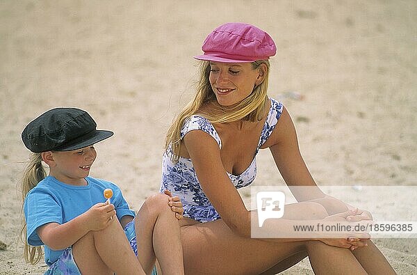 Woman with girl  sitting on sandy beach  mother and daughter