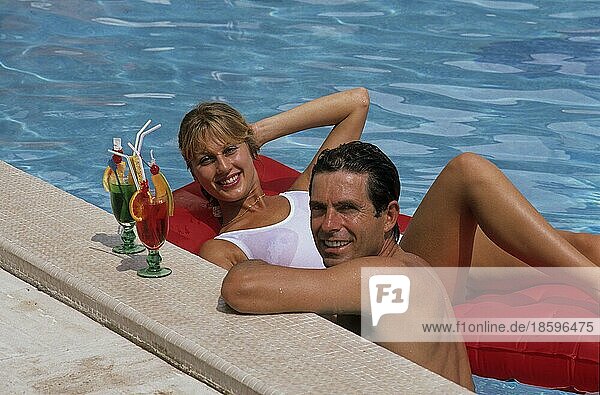 Young couple at the pool  woman lying on air mattress man at the edge of the pool  with cocktail