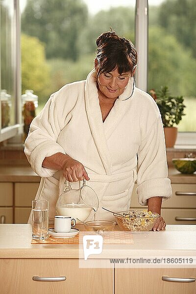 Frau beim Frühstück  bereitet Müsli zu  Frühstück  frühstücken  Kanne Milch  Schüsseln  Müsli  Tasse Kaffee  Glas Wasser  frühstückt  zubereiten  gießen  schütten