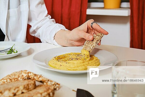 Weibliche Hand taucht ein Stück Knäckebrot in eine Schüssel mit Hummus