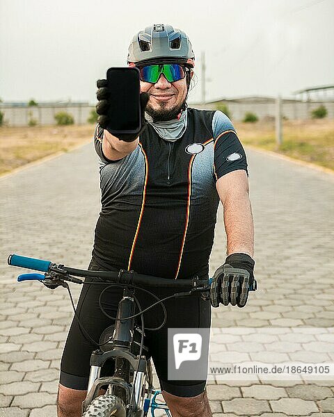 Lächelnder Radfahrer  der eine Werbung auf dem Handy zeigt  Radfahrer in Sportkleidung  der den Bildschirm des Telefons zeigt. Männlicher Radfahrer auf dem Fahrrad zeigt Handybildschirm im Freien
