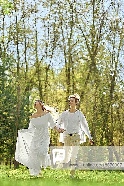Happy newlyweds holding hands and running across the lawn in sunny day