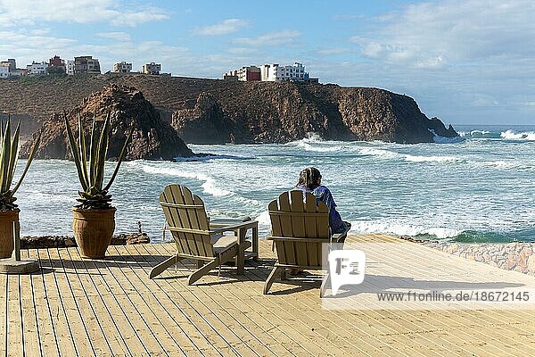 Woman sitting looking out to sea from decking at Hotel auberge Dar Najmat  Mirleft  southern Morocco  north Africa