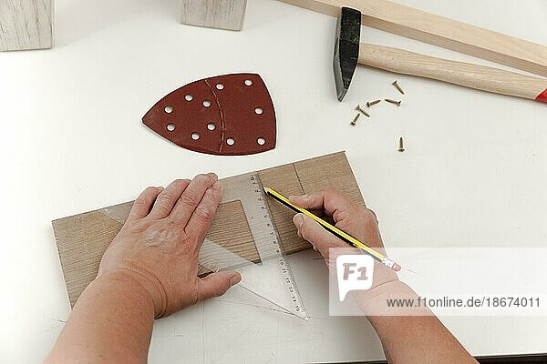 Die Hände einer Frau  die mit einem Winkel und einem Bleistift auf einem weißen Tisch in ihrer Holzwerkstatt Linien auf einem Stück Holz anzeichnet