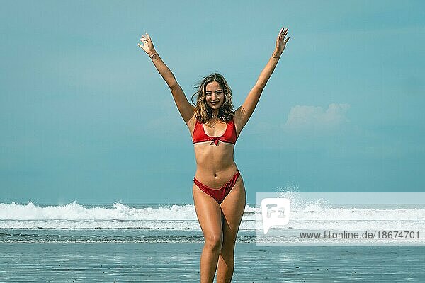 Beautiful young woman in red bikini on a turquoise water beach raising her arms  enjoying the sea  outdoor life  holidays