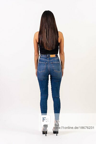 Brunette woman in casting photos on a white background  in jeans and a black t-shirt with her back turned
