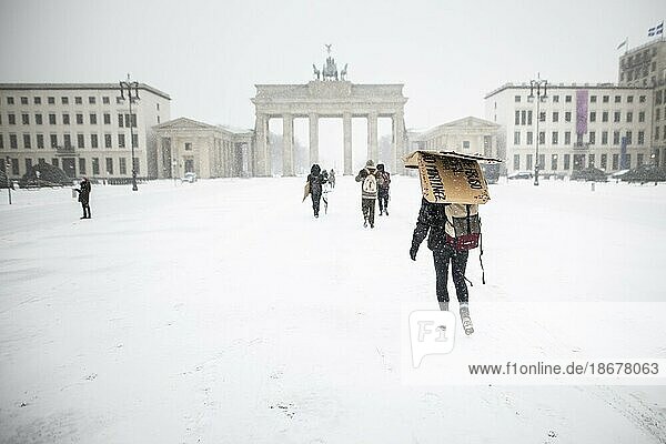 Berlin  Eine Person schützt sich mit einer Pappe  aufgenommen auf dem Pariser Platz vor dem Brandenburger Tor nach während starken Schneefalls in Berlin