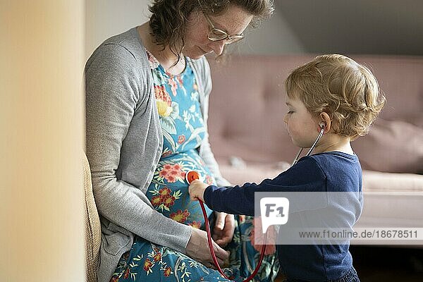 Subject: Family planning. Child listening with a stethoscope on the pregnant mother's belly.  Bonn  Germany  Europe