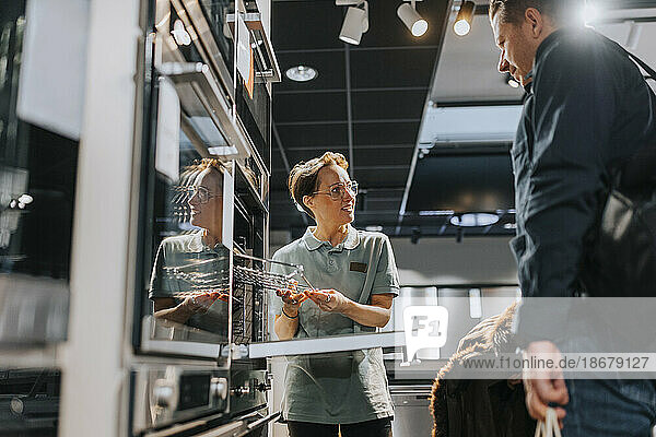 Ein Kunde betrachtet einen Mikrowellenherd  während eine Verkäuferin in einem Elektronikgeschäft hilft