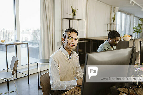 Porträt eines jungen männlichen Programmierers  der an einem Computertisch im Büro sitzt