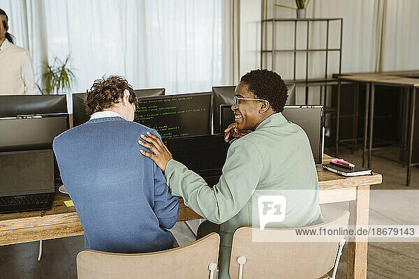 Rückansicht einer lächelnden Programmiererin  die mit einem männlichen Kollegen an einem Computertisch im Büro sitzt
