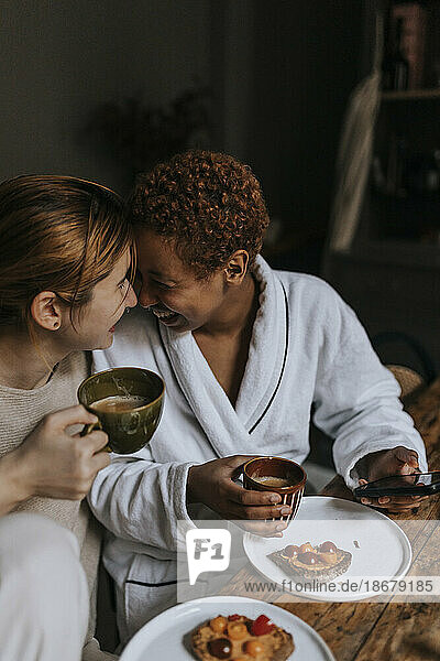 Happy non-binary couple enjoying while having breakfast at home
