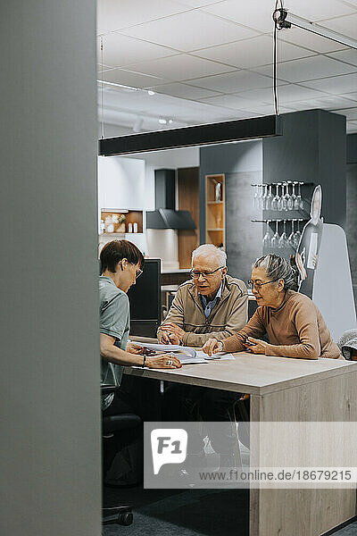 Ein älteres Ehepaar diskutiert mit einer Innenarchitektin an einem Schreibtisch im Geschäft