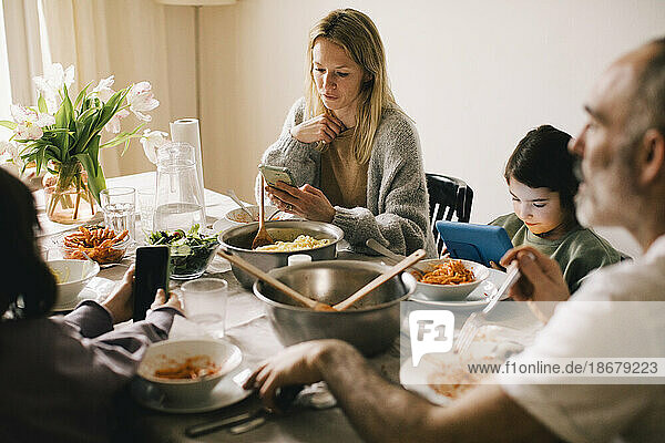 Family using gadgets while sitting at dining table