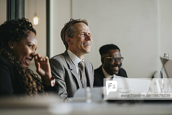 Lächelnder reifer Geschäftsmann  der während einer Sitzung im Sitzungssaal im Büro diskutiert