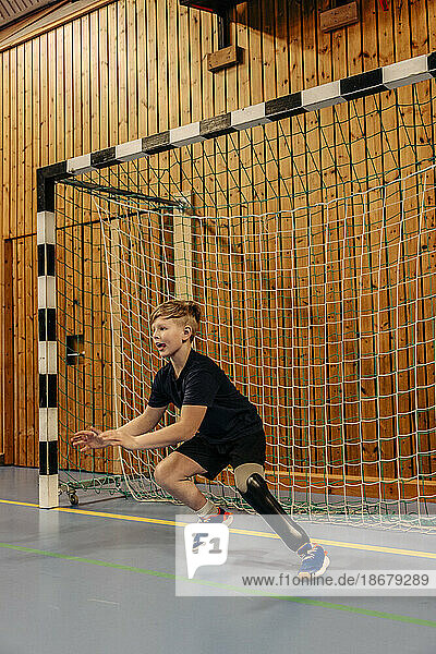 Junge mit Behinderung  der beim Fußballspielen auf dem Sportplatz ein Tor in der Nähe des Netzes erzielt