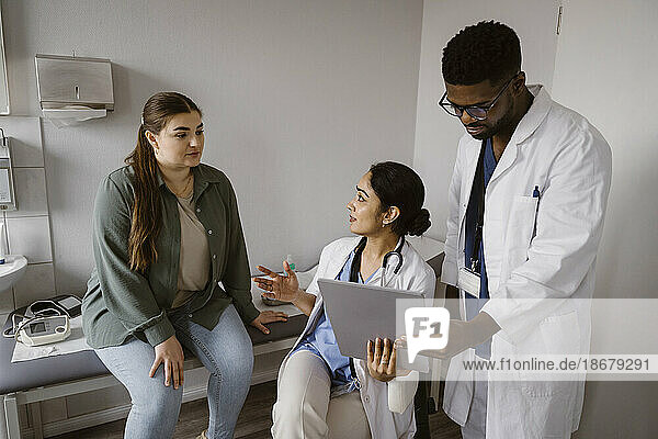 Arzt mit Tablet-PC im Gespräch mit einer Patientin  die auf einem Bett in einer Klinik sitzt