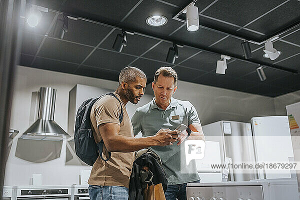 Salesman and mature man discussing over smart phone in appliances store