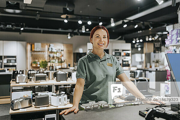 Portrait of smiling female sales clerk standing at counter in electronics store