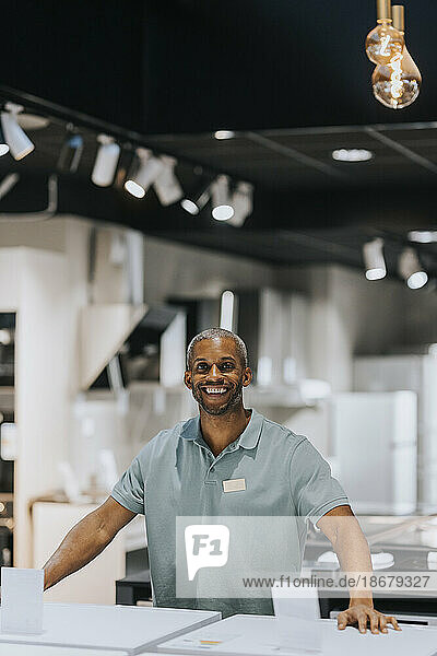 Portrait of happy mature salesman standing at counter in electronics store