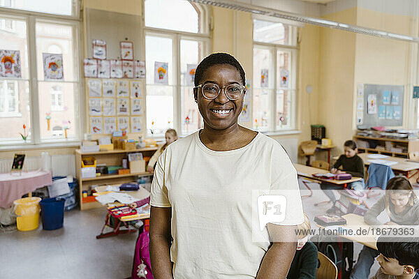 Porträt eines lächelnden Lehrers  der vor den Schülern im Klassenzimmer steht