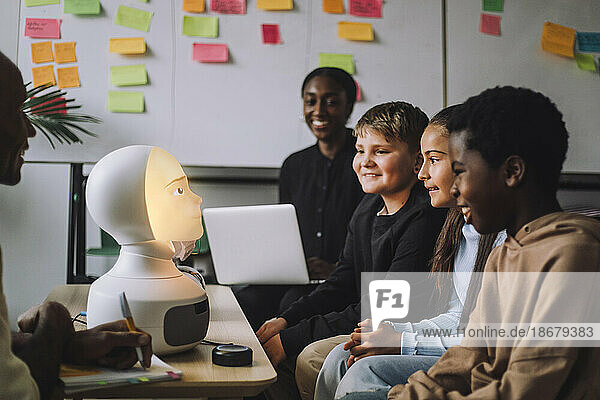 Lächelnde  gemischtrassige Studenten betrachten einen beleuchteten modernen Roboter im Innovationslabor