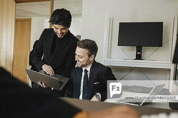 Lächelnder Geschäftsmann  der einem männlichen Kollegen im Büro seinen Laptop erklärt