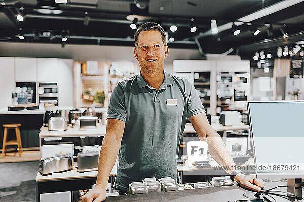 Portrait of smiling mature salesman standing at counter in electronics store
