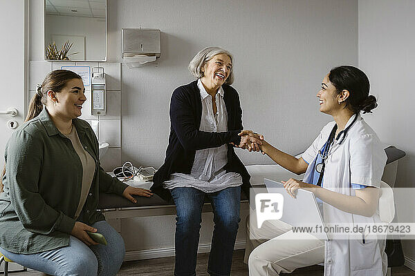 Happy senior woman shaking hand with doctor sitting in clinic