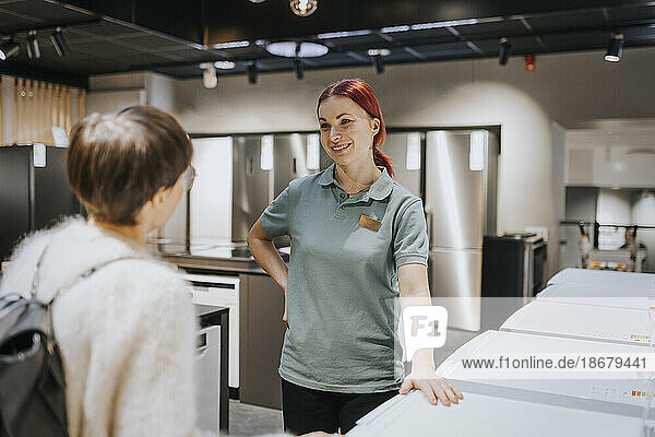 Smiling saleswoman advising female customer in buying appliance at electronics store
