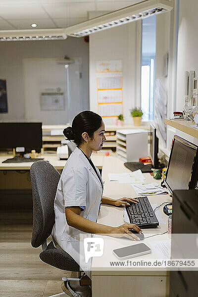 Seitenansicht einer Mitarbeiterin des Gesundheitswesens  die an einem Computer arbeitet  sitzend in einer Klinik