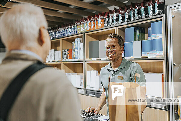 Smiling sales clerk talking with customer at checkout in electronics store