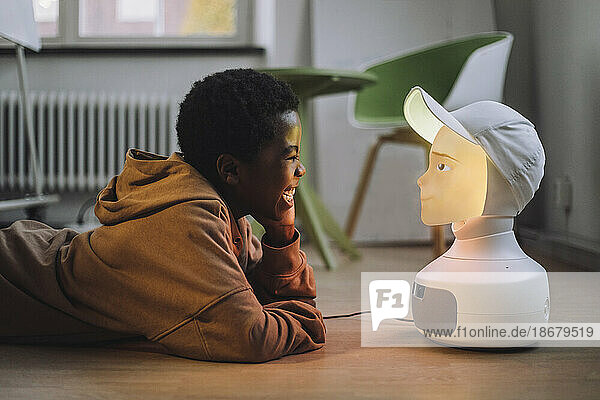 Fröhlicher Junge vor einem beleuchteten KI-Roboter  der im Innovationslabor auf dem Boden liegt