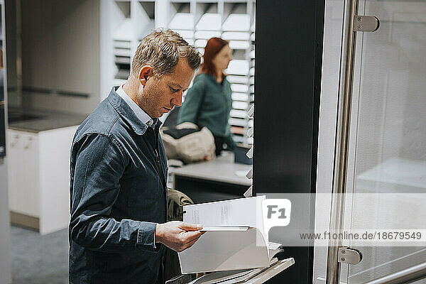 Seitenansicht eines reifen Mannes  der in einem Elektronikgeschäft eine Broschüre liest