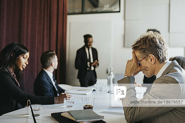 Seitenansicht eines Geschäftsmannes mit dem Kopf in der Hand während einer Besprechung mit Kollegen im Sitzungssaal eines Büros
