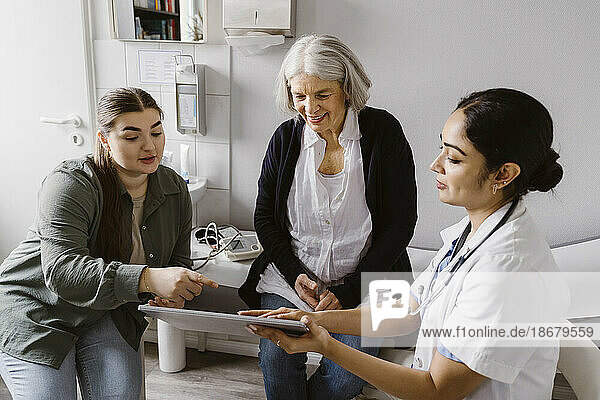 Arzt bespricht sich mit älterer Frau und Tochter über Tablet-PC in der Klinik