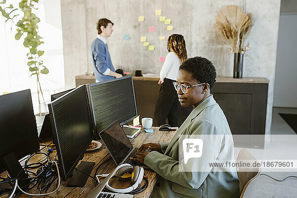 Side view of female programmer working on computer at desk in creative office