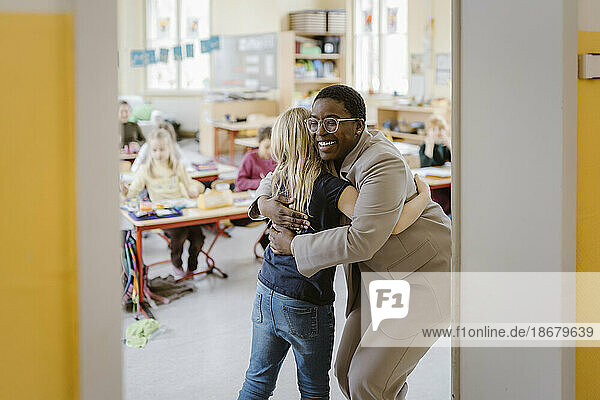 Lächelnde Lehrerin und Schülerin umarmen sich an der Tür im Klassenzimmer