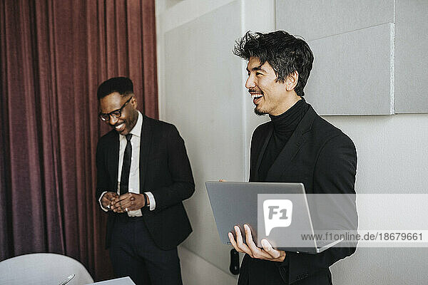Glücklicher Geschäftsmann  der einen Laptop von einem männlichen Kollegen während einer Besprechung im Büro hält