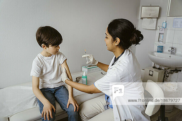 Seitenansicht einer Kinderärztin  die einem Jungen auf dem Bett sitzend in einem Krankenhaus einen Impfstoff verabreicht