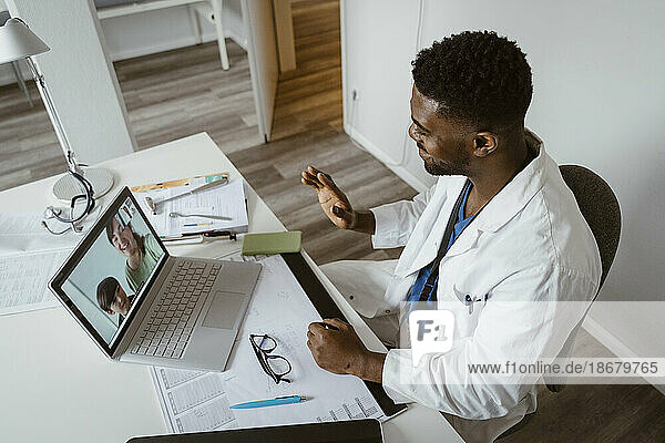 Hoher Blickwinkel eines männlichen Kinderarztes  der Patienten per Videoanruf auf einem Laptop im Gesundheitszentrum begrüßt