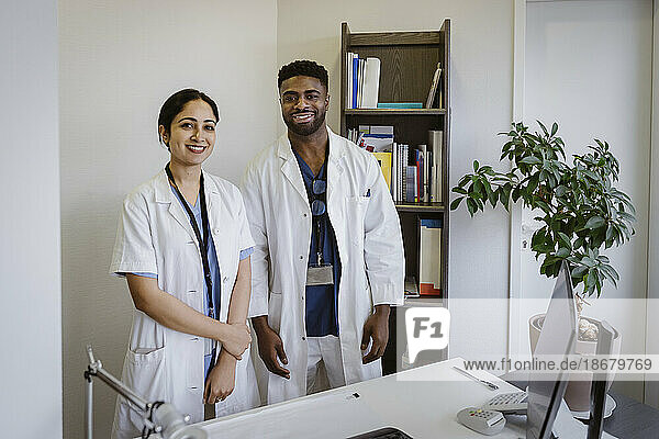 Porträt einer selbstbewussten Frau und eines selbstbewussten Mannes aus dem Gesundheitswesen  die am Schreibtisch einer Klinik stehen