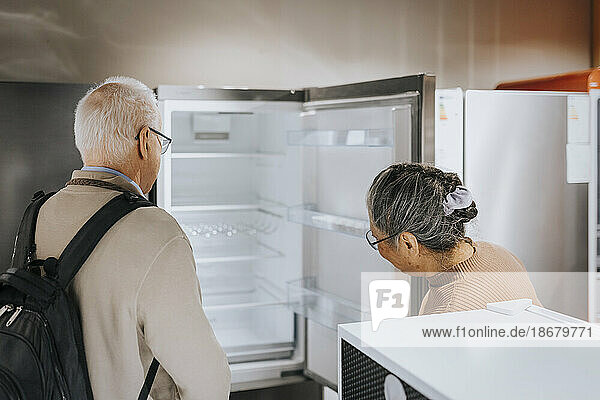 Älteres Ehepaar öffnet und untersucht den Kühlschrank beim Einkaufen in einem Haushaltswarengeschäft