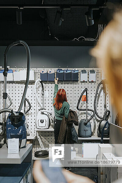 Rückansicht einer Kundin  die beim Einkaufen in einem modernen Elektronikgeschäft Geräte begutachtet