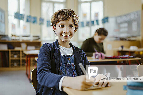 Portrait of smiling schoolboy sitting at desk in classroom