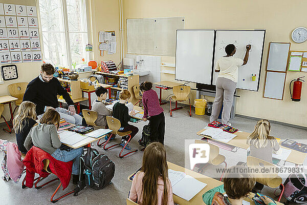 Männlicher und weiblicher Lehrer unterrichten Schüler am Schreibtisch sitzend im Klassenzimmer