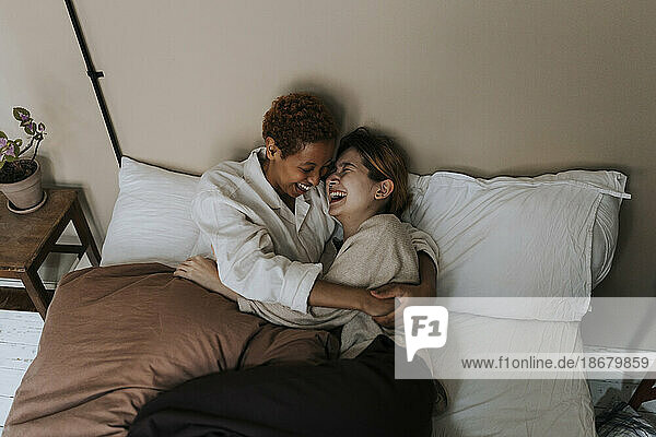 Nicht-binäres Paar  das sich zu Hause auf dem Bett liegend miteinander vergnügt