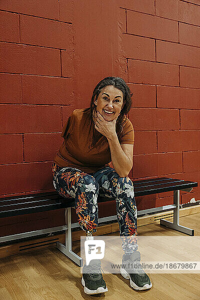 Porträt einer glücklichen Sportlerin mit amputiertem Bein  die auf einer Bank auf einem Sportplatz sitzt
